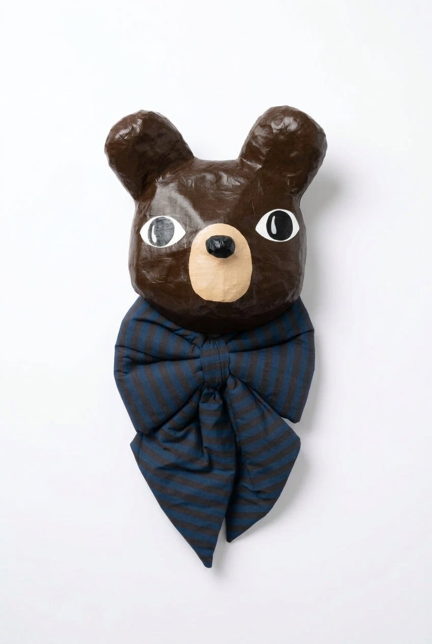 A decorative bear head wall hanging or sculpture with a glossy dark brown finish, large white eyes with black outlines, a beige snout and ear interiors, and a dark blue bow tie with thin red stripes, shown against a plain white background.