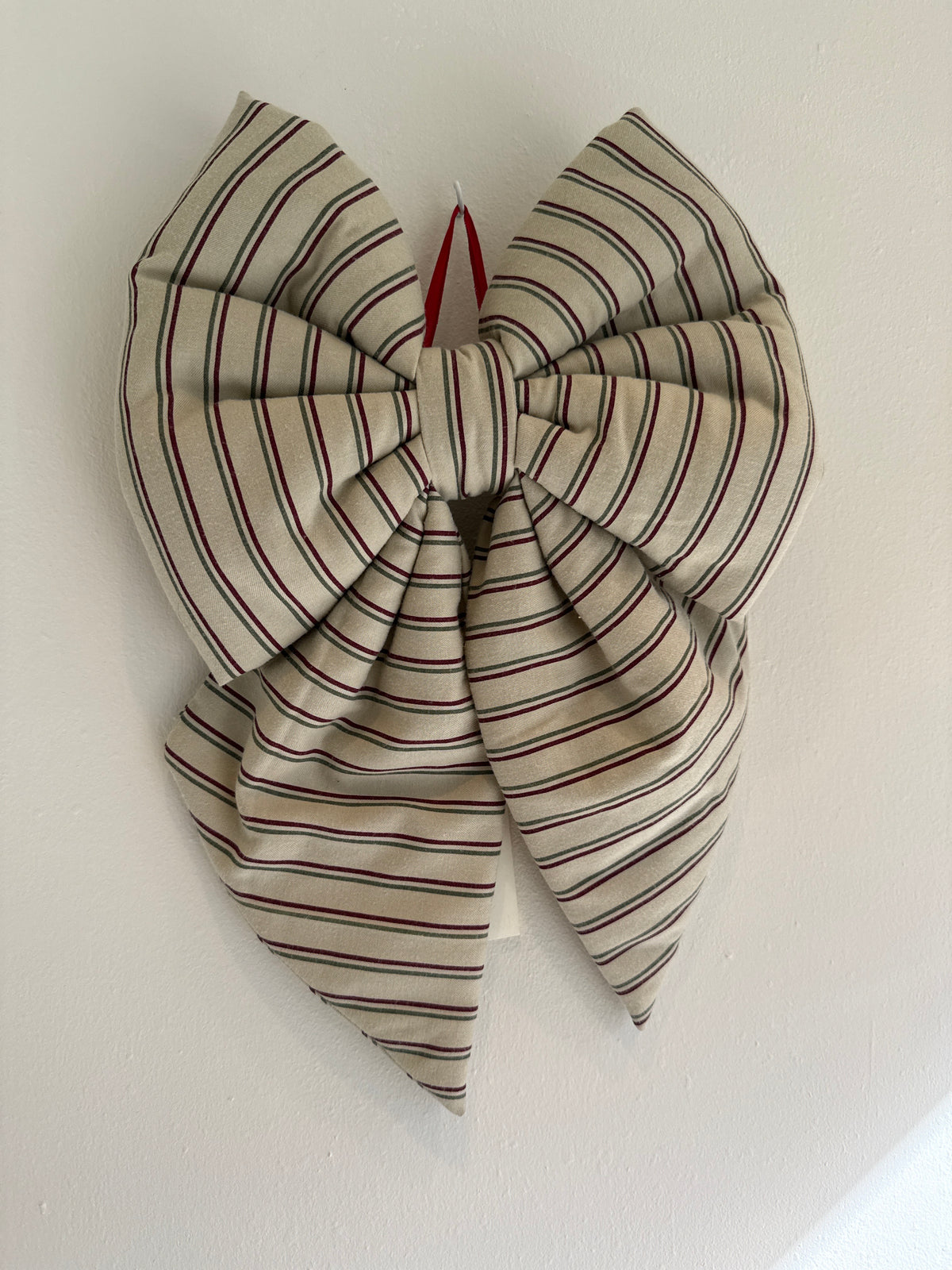A fabric hair bow with a beige base and thin dark brown stripes, featuring a red elastic band visible on the left side, set against a plain white background.