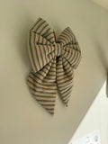 A large fabric bow with thin vertical stripes in beige, brown, and black, hanging on a plain off-white wall.