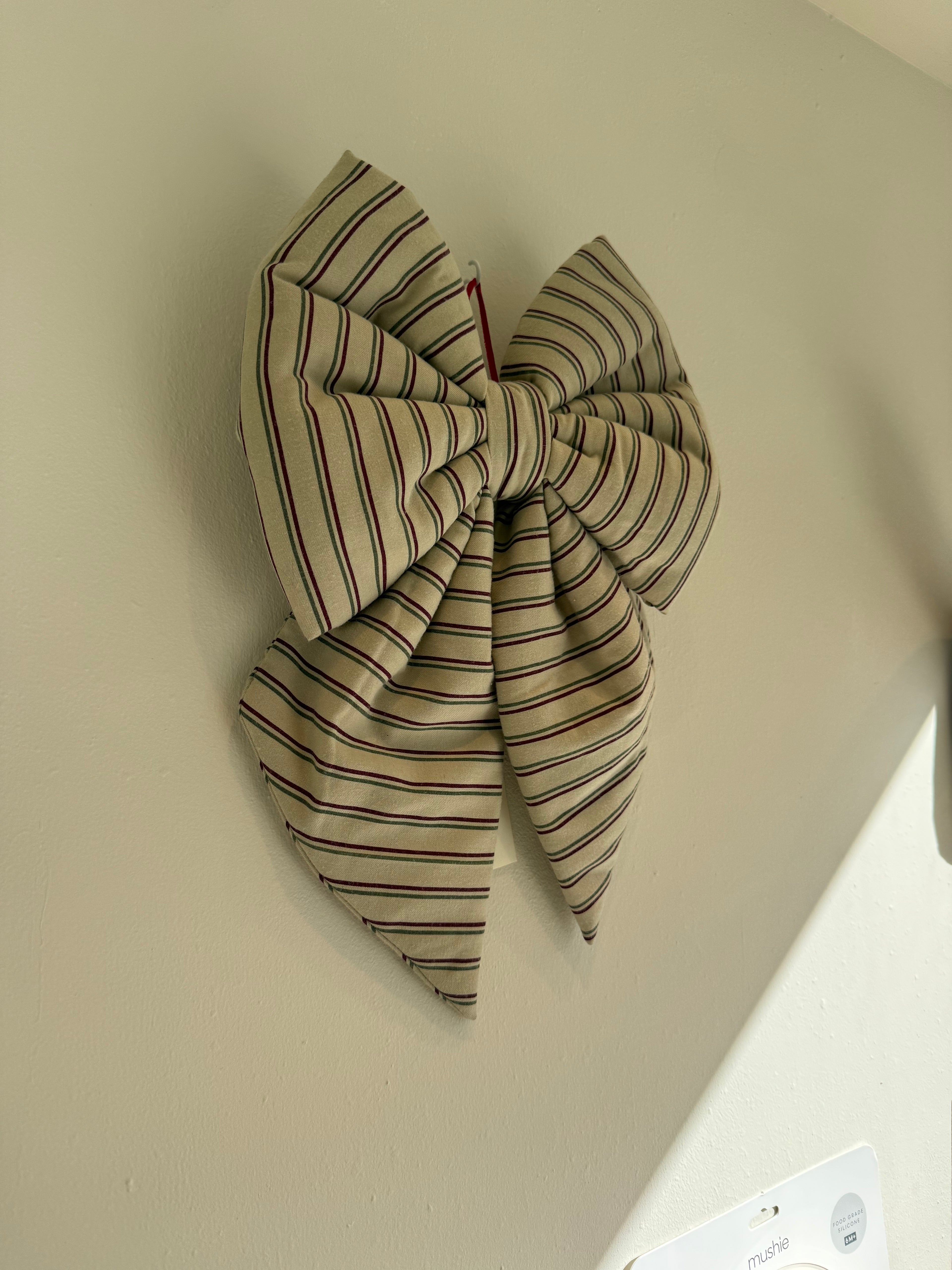 A large fabric bow with thin vertical stripes in beige, brown, and black, hanging on a plain off-white wall.