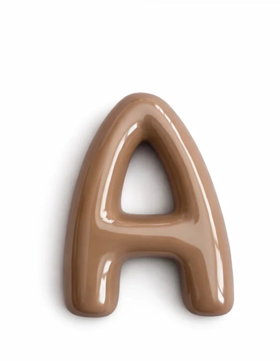 A glossy, 3D decorative letter 'A' in a warm light brown or taupe color, shown on a plain white background.