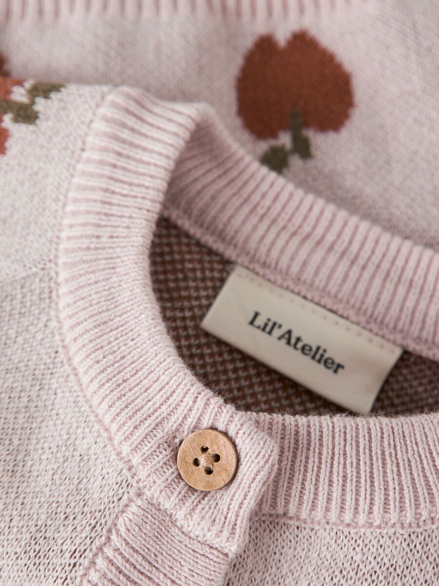Close-up of a pink knitted garment with a button and 'Lil' Atelier' label.