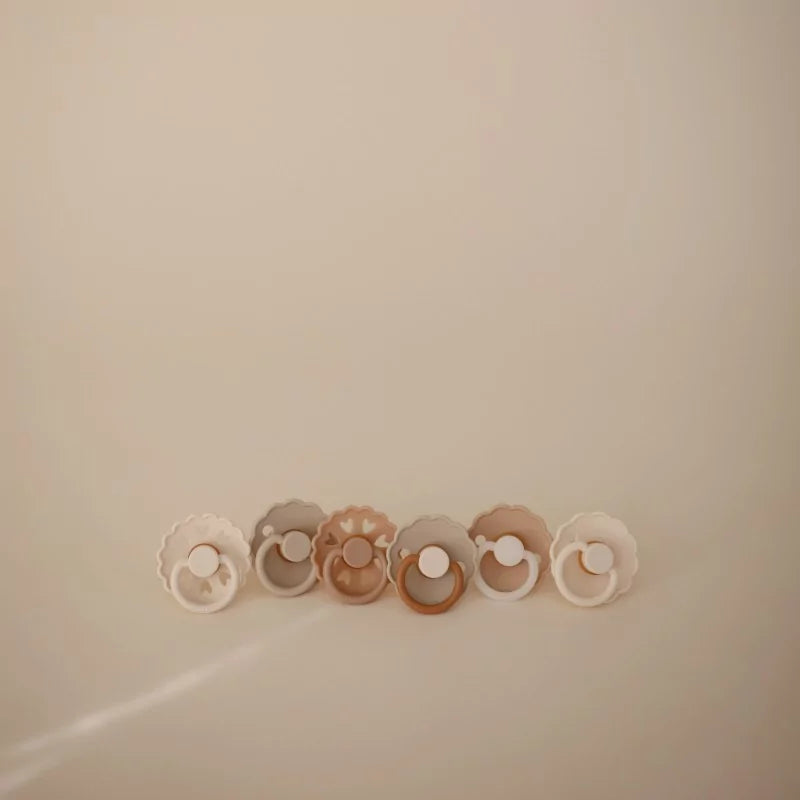 Set of baby pacifiers in various colors on a beige background