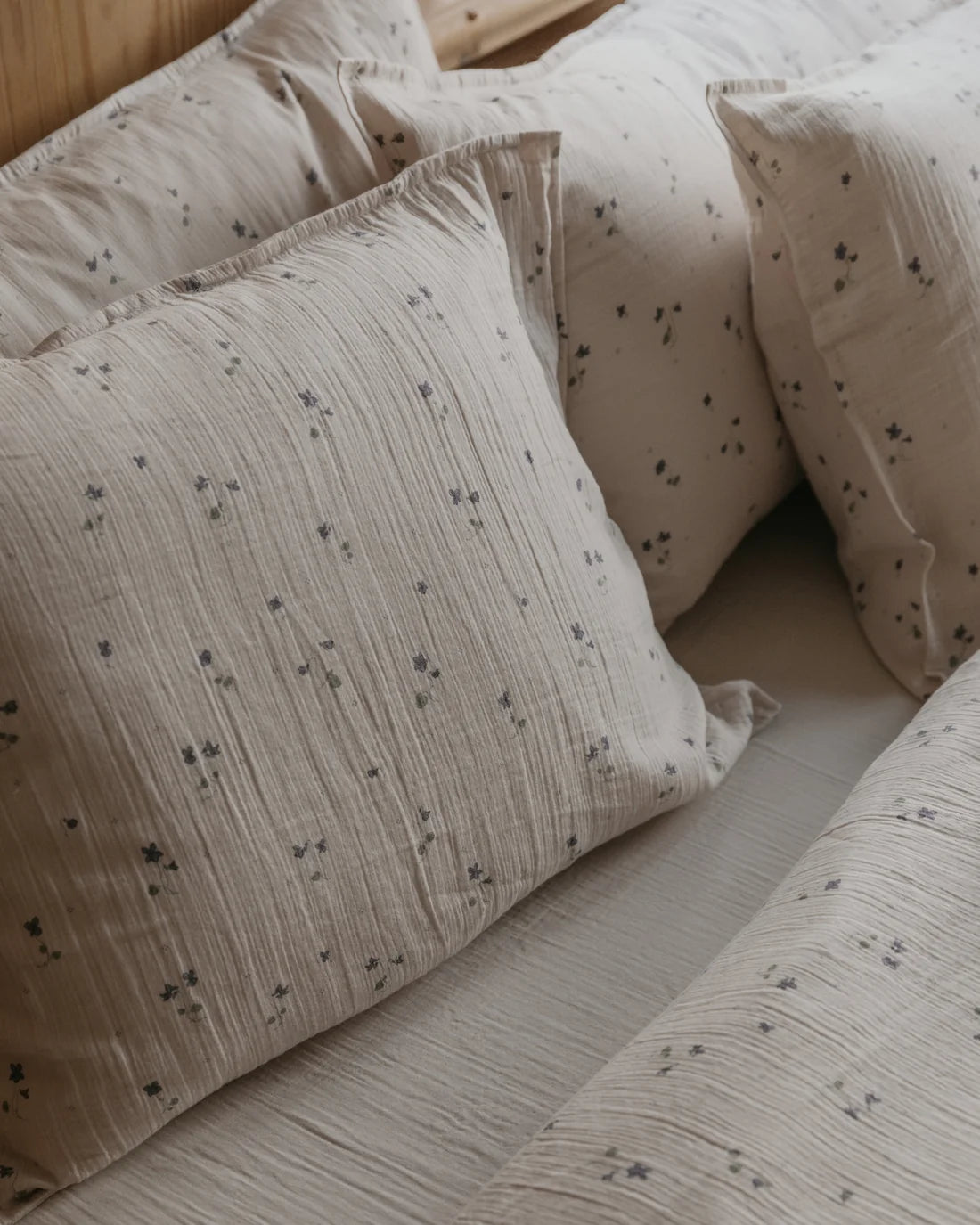 Close-up of textured cotton pillowcases and a matching pillow in a warm beige color with a small scattered floral print, styled on a bed.