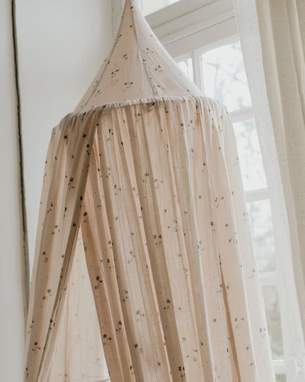 Beige canopy with small  patterns hanging in a room with a window.