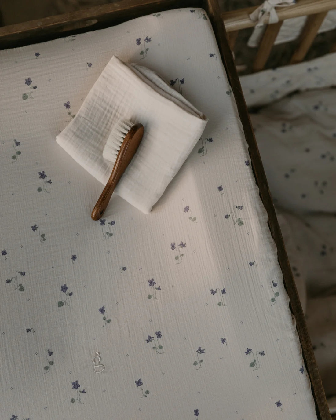 Wooden baby brush and cloth on a crib with floral patterned sheet