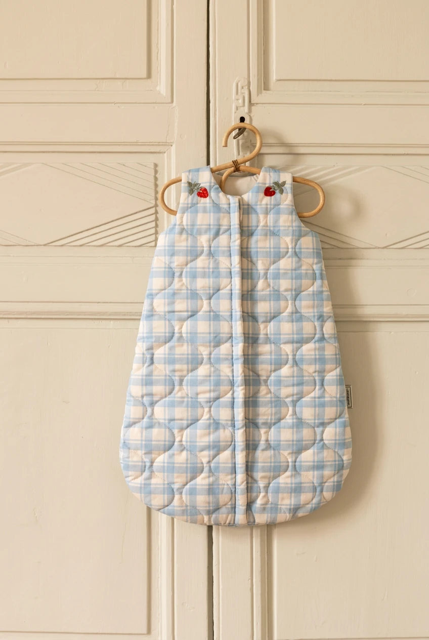 Blue quilted baby sleeping bag hanging on a door handle against a gray paneled wall.