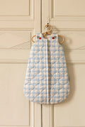 Blue quilted baby sleeping bag hanging on a door handle against a gray paneled wall.