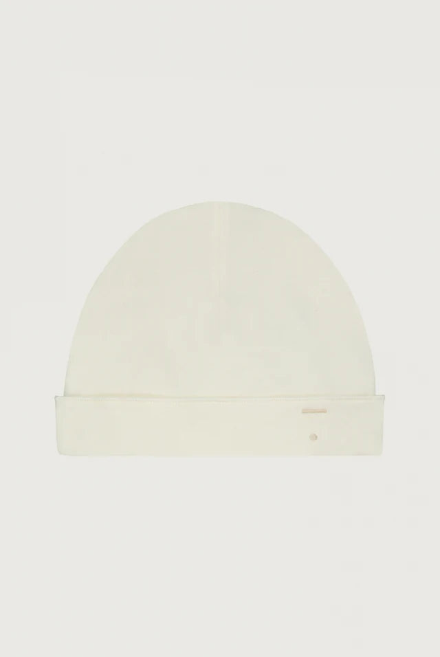 A cream-colored knit beanie hat with a folded cuff, shown flat against a solid off-white background.