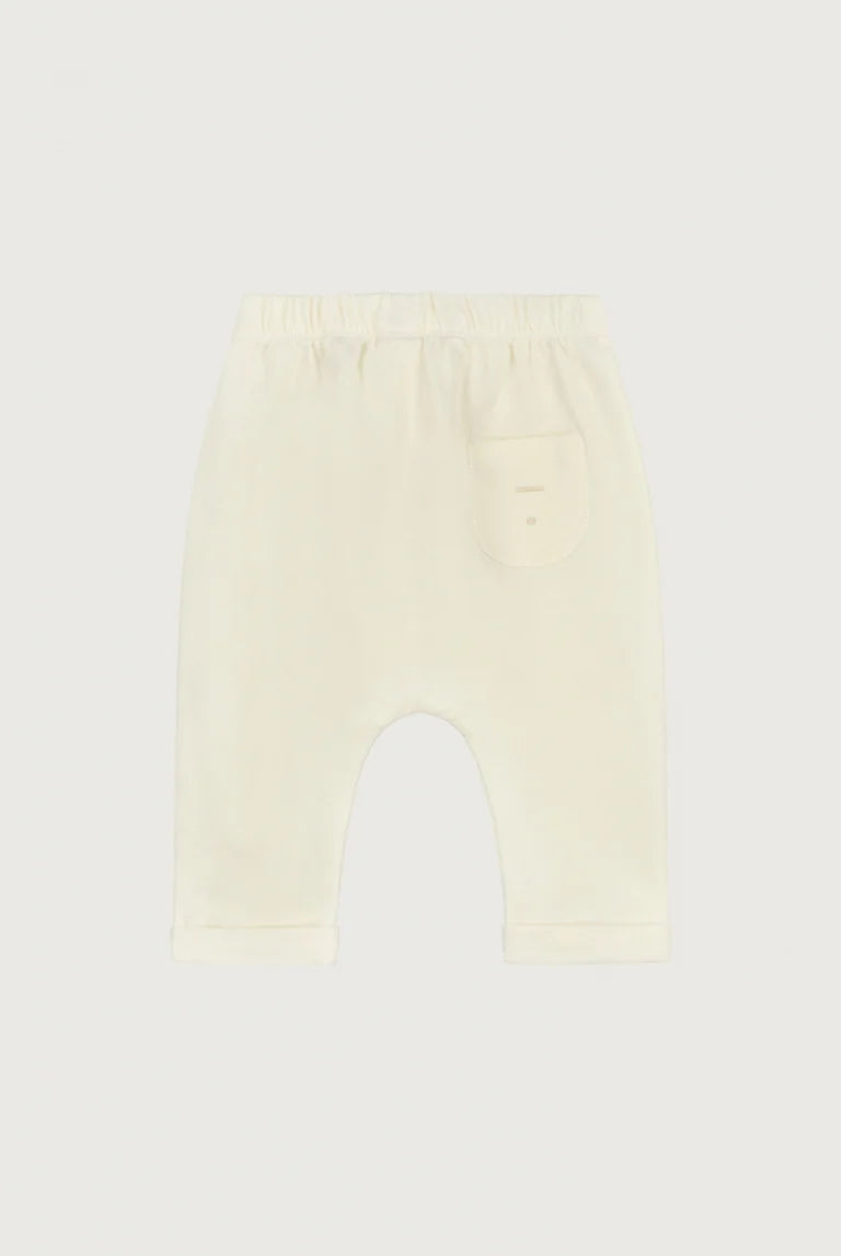 A pair of cream-colored baby pants with an elastic waistband and a small side pocket, shown flat against a light gray background.