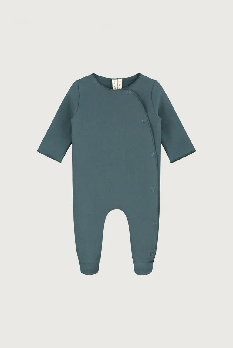 A baby long-sleeve footless one-piece romper in a muted slate blue-gray color, featuring an asymmetrical snap closure and ribbed cuffs and hem, shown against a light gray background.