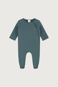 A baby long-sleeve footless one-piece romper in a muted slate blue-gray color, featuring an asymmetrical snap closure and ribbed cuffs and hem, shown against a light gray background.