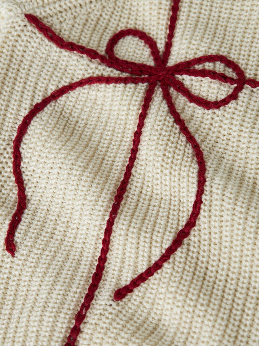 Close-up of a cream-colored knitted fabric with a decorative dark red knotted bow stitched on top.