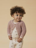 Child wearing a pink knitted cardigan on a beige background
