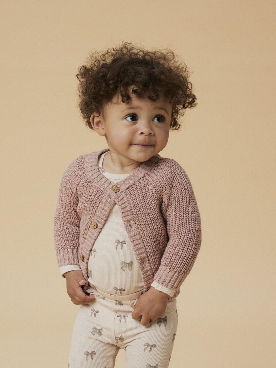 Child wearing a pink knitted cardigan on a beige background