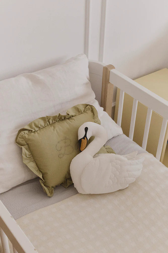 Crib with a swan-shaped pillow and a green cushion on a white background