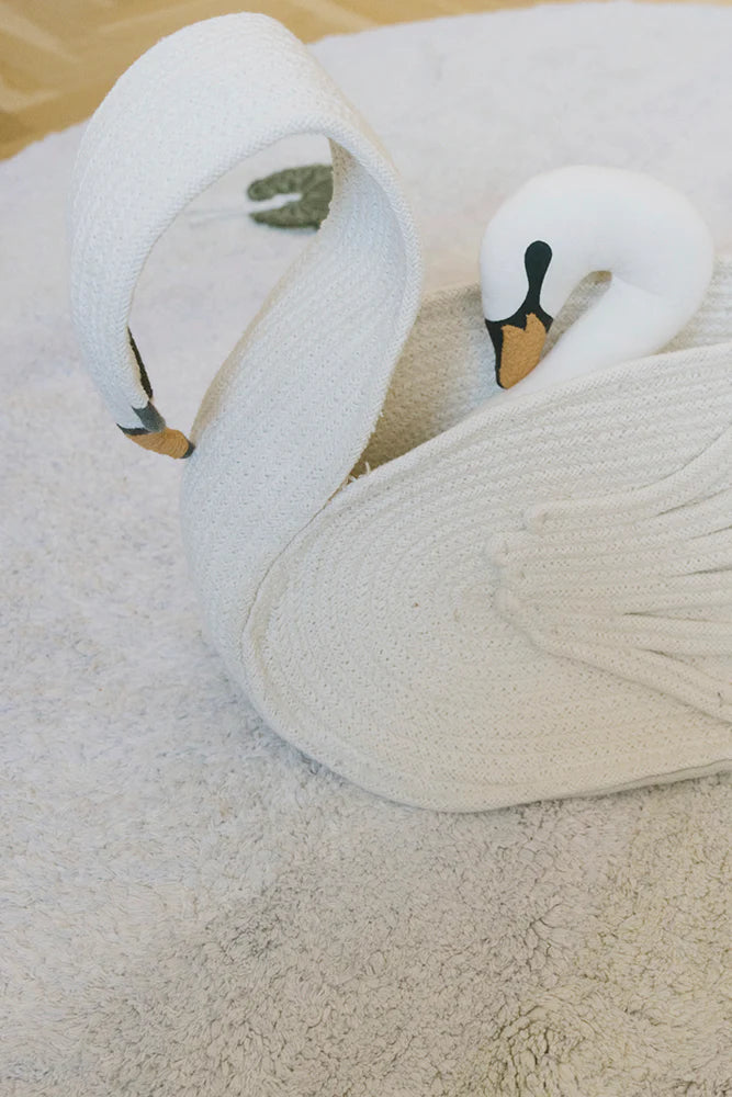 Two white swans lying on a sandy surface