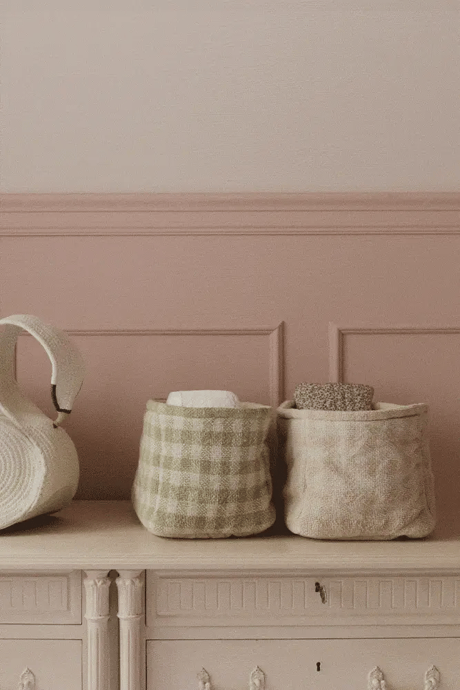 Three fabric baskets on a wooden surface against a pink wall.