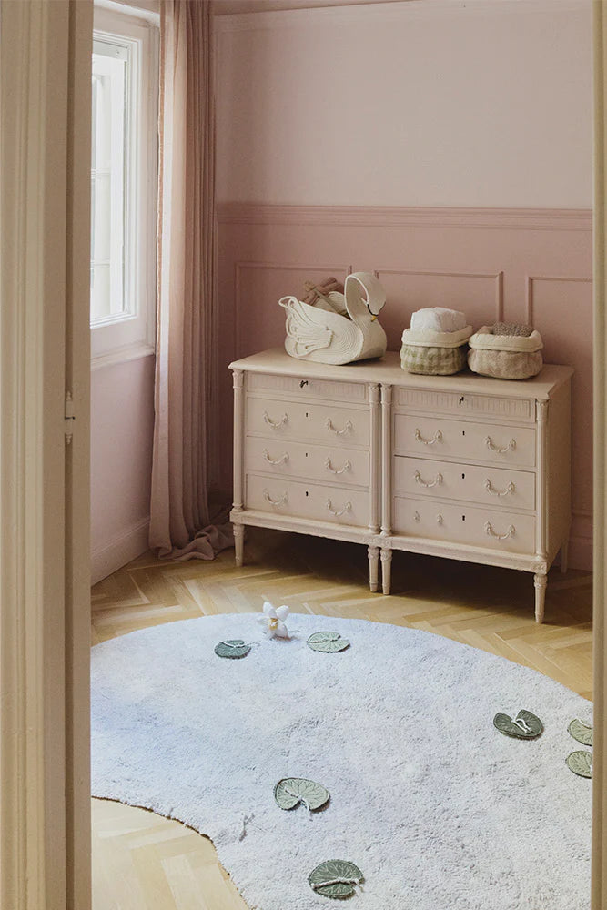 Beige dresser with decorative items against a pink wall in a room with a light blue rug.