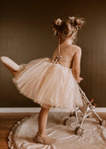 Young girl in a beige dress twirling with a baby stroller on a wooden floor.