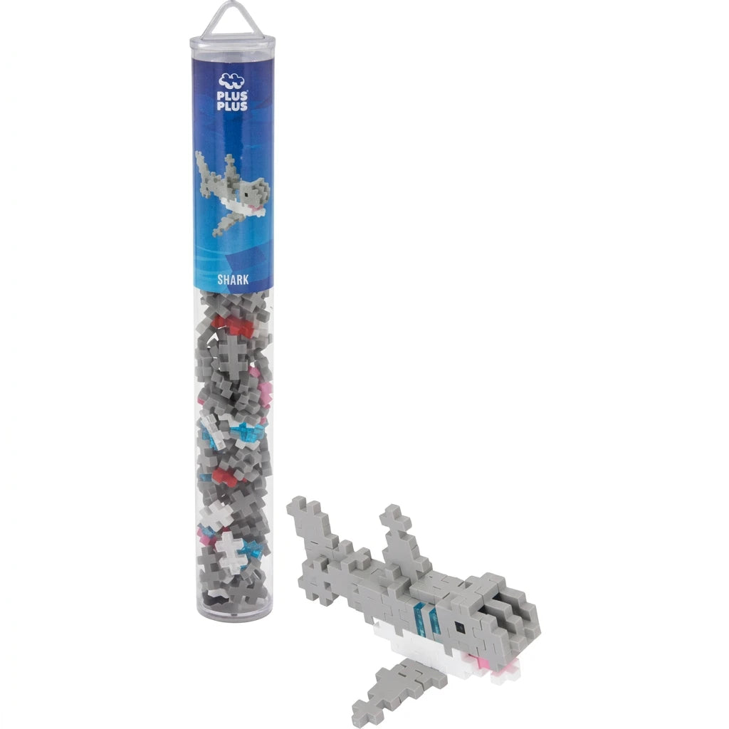 A small shark-shaped building block toy shown beside its clear cylindrical packaging tube on a white background. The tube has a blue label with shark graphics and the brand name Blue Beasts.