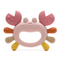 A baby teether toy shaped like a smiling crab, made of soft silicone. The main body is light pink, with pink claws decorated with embossed stars and dots, orange spiral accents on the sides, beige textured pads, and yellow feet, all set against a plain white background.