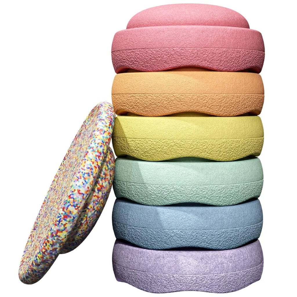 A stack of six textured circular foam discs in pink, orange, yellow, mint green, light blue, and lavender, with a seventh multicolor-speckled disc leaning against the stack on a white background.