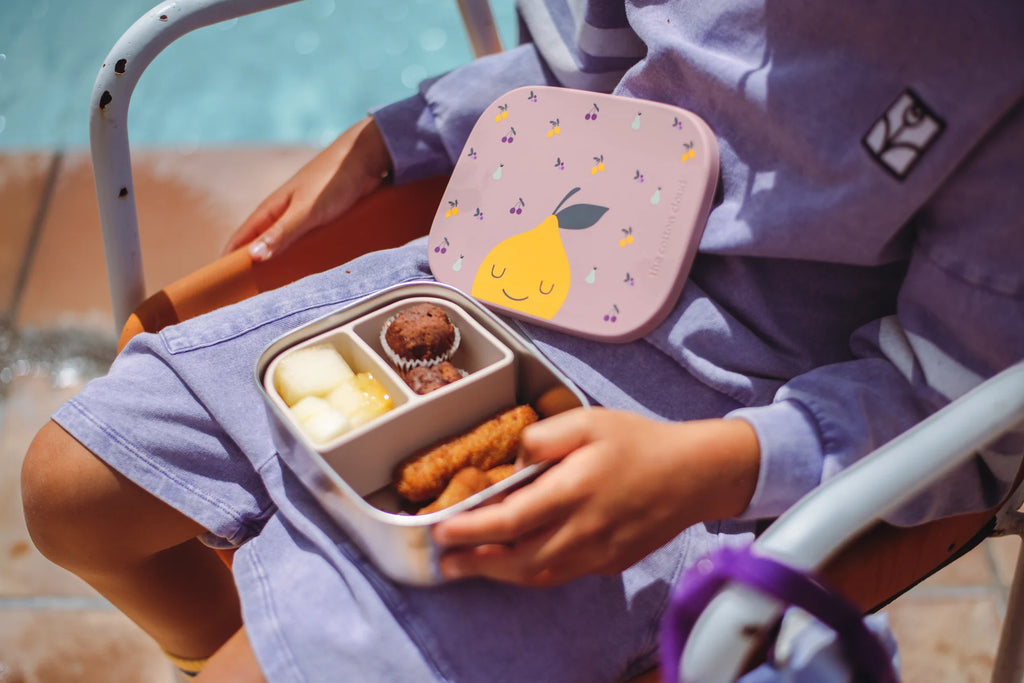 Person holding a bento box with food by a poolside