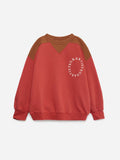 A colorblock crewneck sweatshirt in red and brown, featuring a circular white graphic print on the left chest that reads 'TRULF BEARSTREY'.