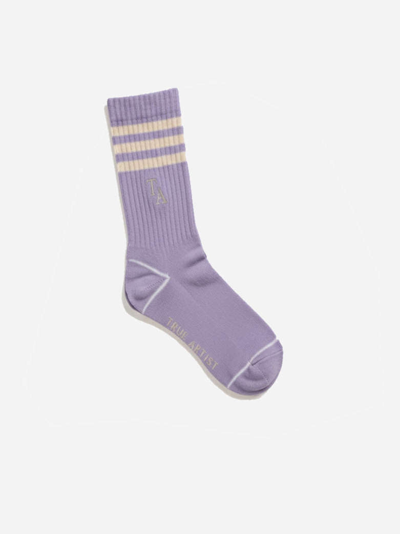 A single lavender crew sock with three cream stripes at the ribbed cuff, a small embroidered logo, and 'TRUE ARTSY' printed on the sole, shown on a light gray background.