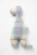 A handmade wool felt dinosaur plush toy in a pastel plaid pattern of light blue, cream, and pink, lying on a wooden floor. A small fabric tag with the brand name 'WOOLD' is visible near the neck.
