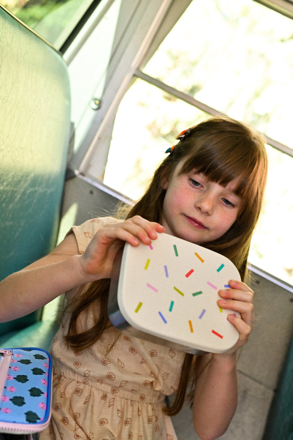 Young girl holding a white plate with colorful sprinkles design indoors.