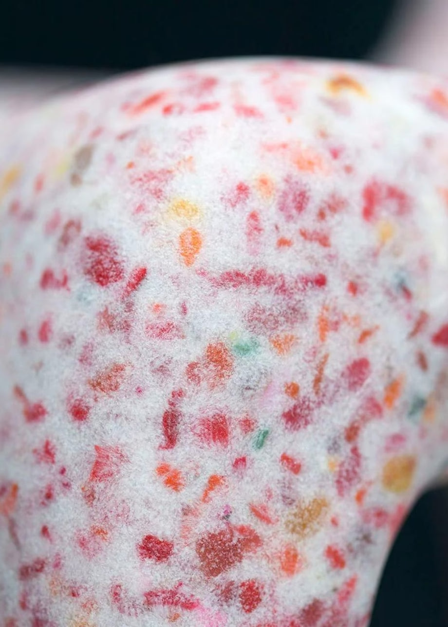 A close-up of a white textured surface covered with small multicolored speckles, including red, orange, yellow, and green, against a dark blurred background.