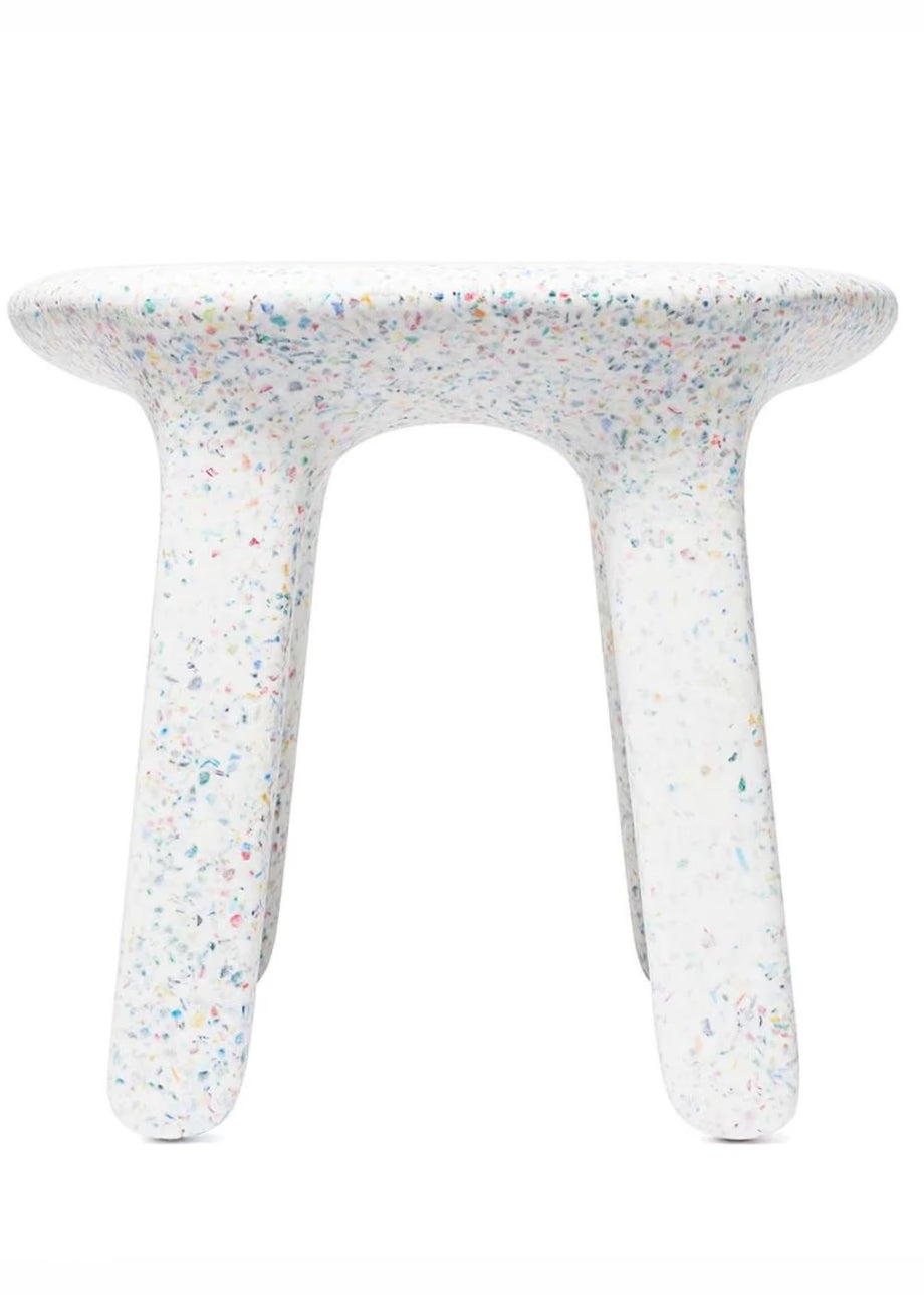 A table with a rounded, thick and legs, featuring a white terrazzo pattern with multicolored flecks, set against a plain white background