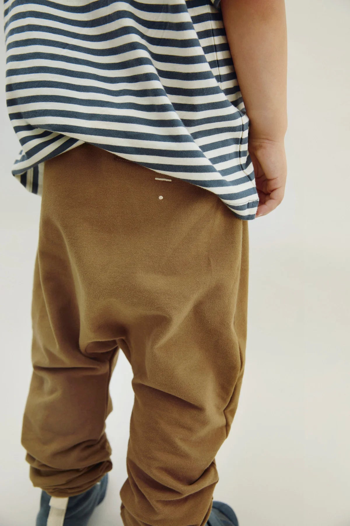 Kid wearing a striped shirt and brown pants on a plain background