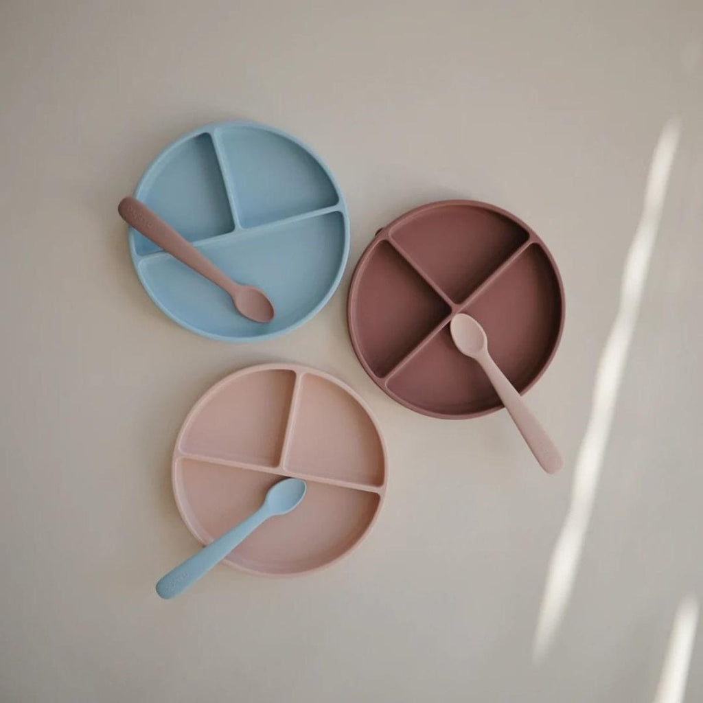 Three divided plates and spoons in pastel colors on a light background