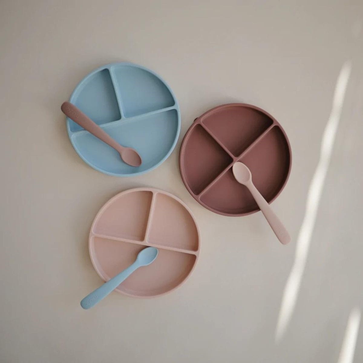 Three divided plates and spoons in pastel colors on a light background