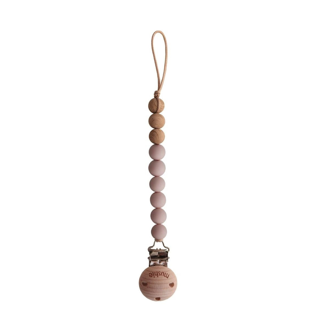 A wooden baby teething ring clip with a loop at the top, featuring a gradient of natural wood, light pink, and dusty rose beads, and a metal clip at the bottom with a wooden ball engraved with the brand name 'mumiyi'.