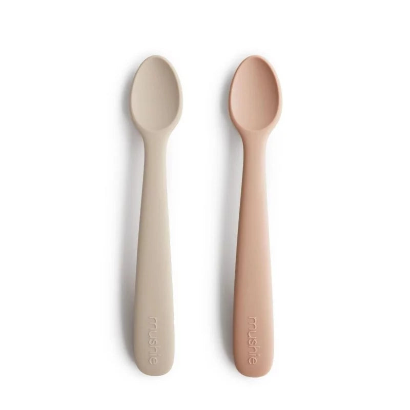 Two silicone spoons, one beige and one blush, on a white background with 'mushie' branding.