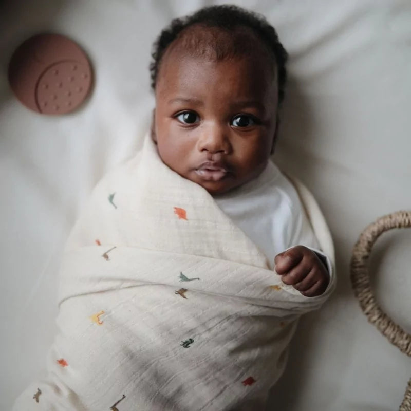 Baby wrapped in a light-colored blanket with small patterns, lying on a white surface.